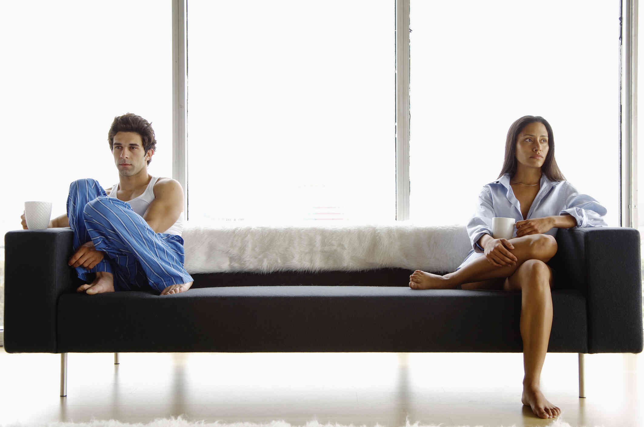 A male and female couple look upset as they sit on opposite sides on  the couch.